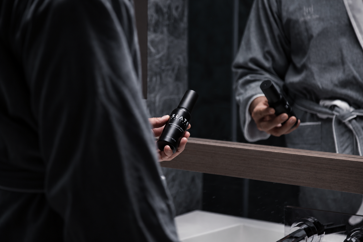 A morning grooming scene featuring SLATE Hair Reset Spray in a dark bathroom.