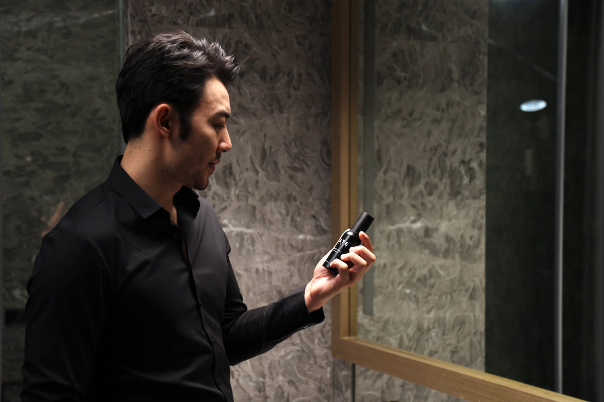 A man holds SLATE Hair Reset Spray beside a bathroom mirror after resetting his hair.