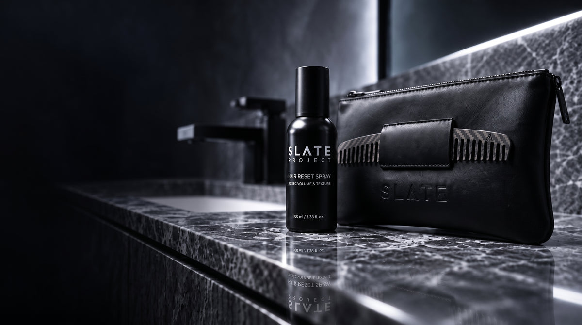 SLATE Hair Reset Spray, carbon-fiber comb and tactical sleeve arranged on a dark marble bathroom counter.