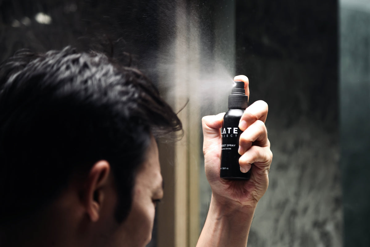 A man applies SLATE Hair Reset Spray with a visible mist during the morning reset protocol.